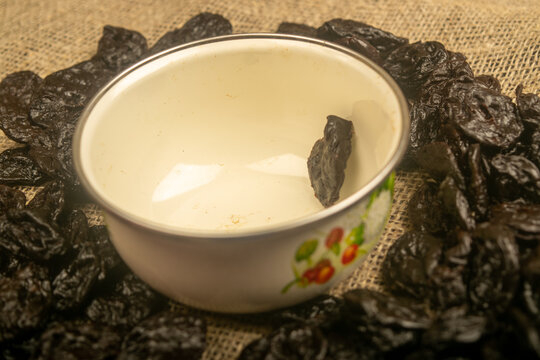 Dried prunes in a metal bowl and dried prunes scattered on a background of coarse-textured burlap. Close up.