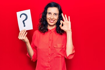 Naklejka premium Young beautiful hispanic woman holding question mark doing ok sign with fingers, smiling friendly gesturing excellent symbol