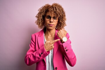 Young african american businesswoman wearing glasses standing over pink background In hurry...