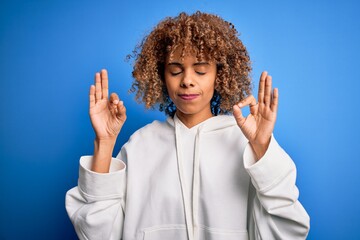 Beautiful african american sporty woman wearing casual sweatshirt over blue background relax and smiling with eyes closed doing meditation gesture with fingers. Yoga concept.