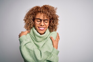 Young beautiful african american woman wearing turtleneck sweater and glasses Hugging oneself happy and positive, smiling confident. Self love and self care