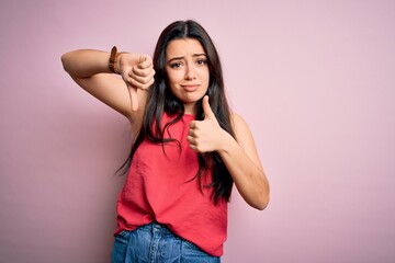 Fototapeta na wymiar Young brunette woman wearing casual summer shirt over pink isolated background Doing thumbs up and down, disagreement and agreement expression. Crazy conflict