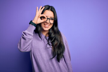 Young brunette woman wearing glasses over purple isolated background doing ok gesture with hand...
