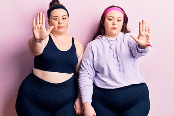 Young plus size twins wearing sportswear doing stop sing with palm of the hand. warning expression with negative and serious gesture on the face.
