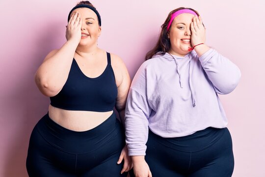 Young plus size twins wearing sportswear covering one eye with hand, confident smile on face and surprise emotion.