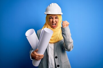 Middle age architect woman wearing muslim hijab and security helmet holding blueprints annoyed and frustrated shouting with anger, crazy and yelling with raised hand, anger concept