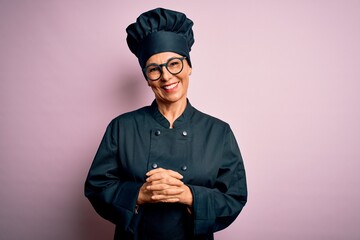 Middle age brunette chef woman wearing cooker uniform and hat over isolated pink background with...
