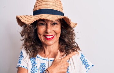 Middle age beautiful brunette woman on vacation wearing summer hat over white background smiling cheerful pointing with hand and finger up to the side