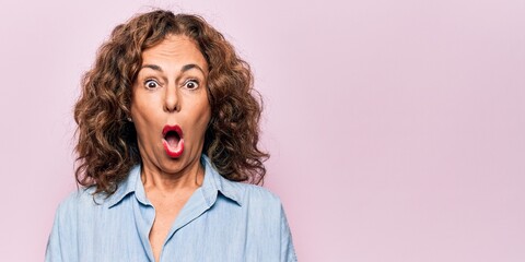 Middle age beautiful woman wearing casual denim shirt standing over pink background afraid and...