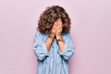 Middle age beautiful woman wearing casual denim shirt standing over pink background with sad...