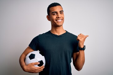 Handsome african american man playing footbal holding soccer ball over white background Pointing to the back behind with hand and thumbs up, smiling confident