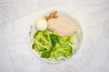 A dish of healthy food with chicken breast and a hard boiled egg and boiled broccoli