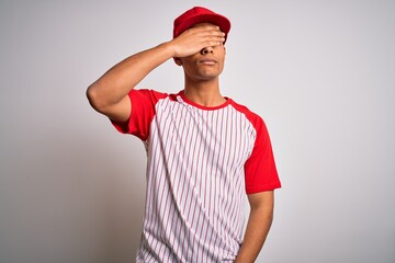 Young handsome african american sportsman wearing striped baseball t-shirt and cap covering eyes with hand, looking serious and sad. Sightless, hiding and rejection concept