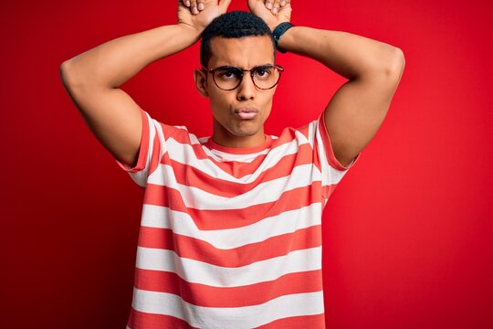 Young handsome african american man wearing casual striped t-shirt and glasses doing funny gesture with finger over head as bull horns