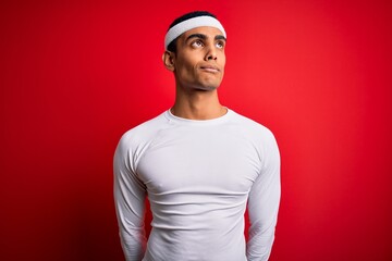 Young handsome african american sportsman wearing sportswear over red background smiling looking to the side and staring away thinking.