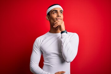 Young handsome african american sportsman wearing sportswear over red background with hand on chin thinking about question, pensive expression. Smiling and thoughtful face. Doubt concept.