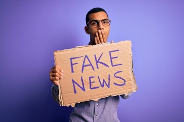 Young handsome african american man protesting holding banner with fake news message cover mouth...