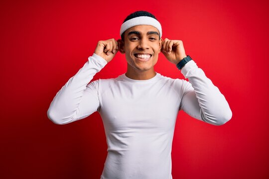 Young handsome african american sportsman wearing sportswear over red background Smiling pulling ears with fingers, funny gesture. Audition problem