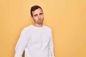 Young handsome man with blue eyes wearing casual sweater standing over yellow background looking sleepy and tired, exhausted for fatigue and hangover, lazy eyes in the morning.