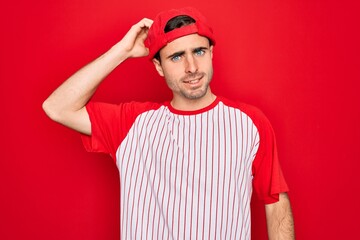 Young handsome sporty man with blue eyes wearing striped baseball t-shirt and cap confuse and wonder about question. Uncertain with doubt, thinking with hand on head. Pensive concept.