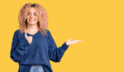 Young blonde woman with curly hair wearing casual winter sweater showing palm hand and doing ok gesture with thumbs up, smiling happy and cheerful