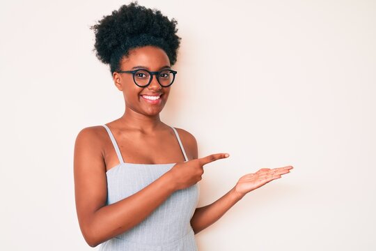 Young african american woman wearing casual clothes and glasses amazed and smiling to the camera while presenting with hand and pointing with finger.