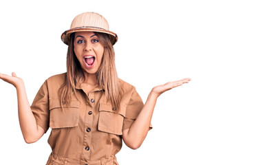 Fototapeta premium Young beautiful woman wearing explorer hat celebrating victory with happy smile and winner expression with raised hands