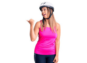 Young beautiful woman wearing bike helmet smiling with happy face looking and pointing to the side with thumb up.