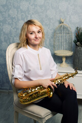 Blonde girl with a saxophone in a chair on photostudio.
