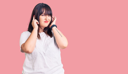 Fototapeta premium Young plus size woman wearing casual clothes covering ears with fingers with annoyed expression for the noise of loud music. deaf concept.