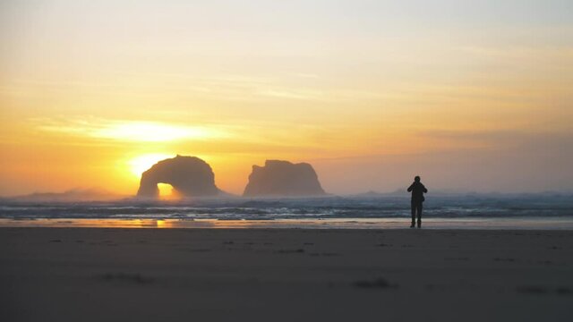 Breathtaking 4k footage of person makes a picture of the rock formation twin rocks at Rockaway Beach rock formation while sunset - magical moment - Oregon sightseeing - places to see - slow motion