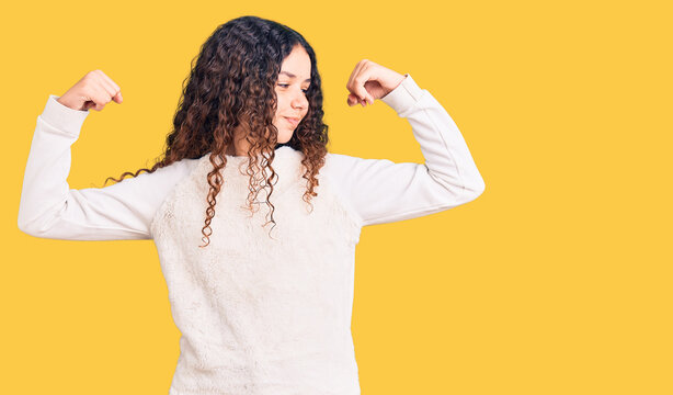 Beautiful kid girl with curly hair wearing casual clothes showing arms muscles smiling proud. fitness concept.