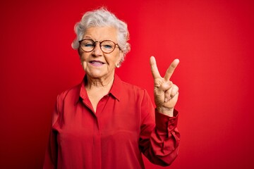 Senior beautiful grey-haired woman wearing casual shirt and glasses over red background showing and pointing up with fingers number two while smiling confident and happy.