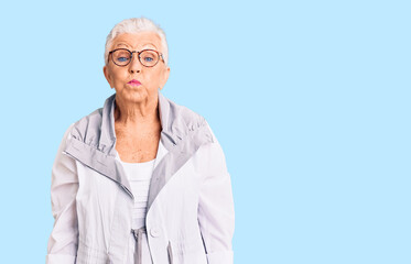 Senior beautiful woman with blue eyes and grey hair wearing casual clothes and glasses making fish face with lips, crazy and comical gesture. funny expression.