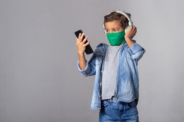 White boy with curly hair wearing protection mask against covid-19 with smartphone listening to music with headphone