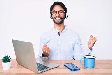 Handsome hispanic man working at the office wearing operator headset celebrating surprised and amazed for success with arms raised and eyes closed