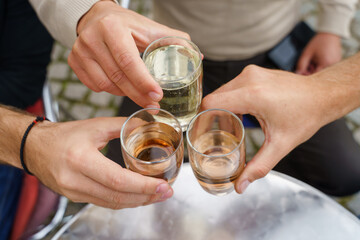 Close up on hands of unknown people holding glasses toasting - Caucasian men celebrating with wine and soda alcohol drink spricer popular in balkan countries - close up top view in day outdoor - obrazy, fototapety, plakaty