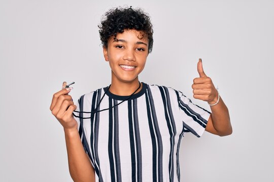 Young beautiful african american afro referee woman wearing striped uniform using whistle happy with big smile doing ok sign, thumb up with fingers, excellent sign