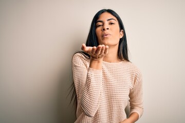 Young beautiful hispanic woman wearing elegant pink sweater over isolated background looking at the camera blowing a kiss with hand on air being lovely and sexy. Love expression.