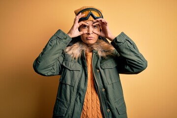 Young beautiful hispanic woman wearing ski glasses and coat for winter weather Trying to open eyes...