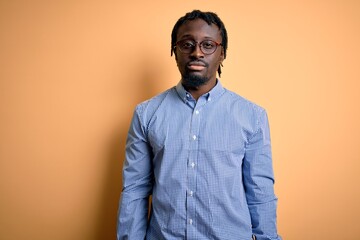Obraz premium Young handsome african american man wearing shirt and glasses over yellow background Relaxed with serious expression on face. Simple and natural looking at the camera.