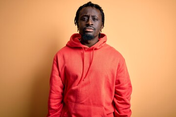 Obraz premium Young african american sporty man wearing sweatshirt with hoodie over yellow background Relaxed with serious expression on face. Simple and natural looking at the camera.
