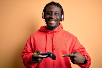 Fototapeta na wymiar Young african american gamer man playing video game using joystick and headphones very happy pointing with hand and finger
