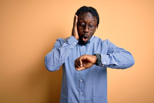 Young Handsome African American Man Wearing Shirt And Glasses Over Yellow Background Looking At The Watch Time Worried, Afraid Of Getting Late