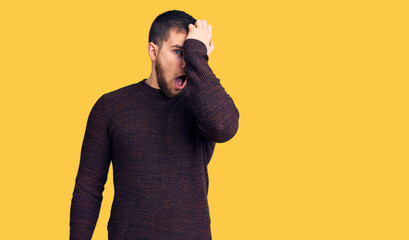 Young handsome man wearing casual sweater surprised with hand on head for mistake, remember error....