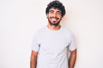 Fototapeta na wymiar Handsome young man with curly hair and bear wearing casual tshirt looking positive and happy standing and smiling with a confident smile showing teeth