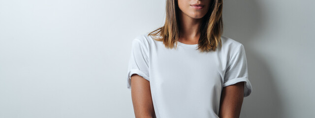 Handsome woman in white blank t-shirt wearing glasses, empty wall, horizontal studio portrait. Wide...