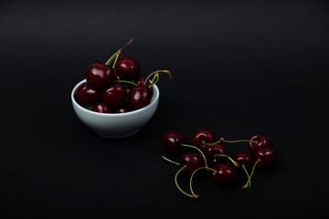 white bowl of black cherries isolated on black background