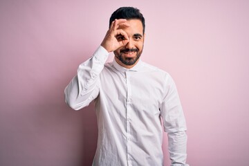 Fototapeta premium Young handsome man with beard wearing casual shirt standing over pink background doing ok gesture with hand smiling, eye looking through fingers with happy face.