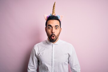 Young handsome man with beard wearing funny unicorn diadem over pink background afraid and shocked with surprise expression, fear and excited face. © Krakenimages.com